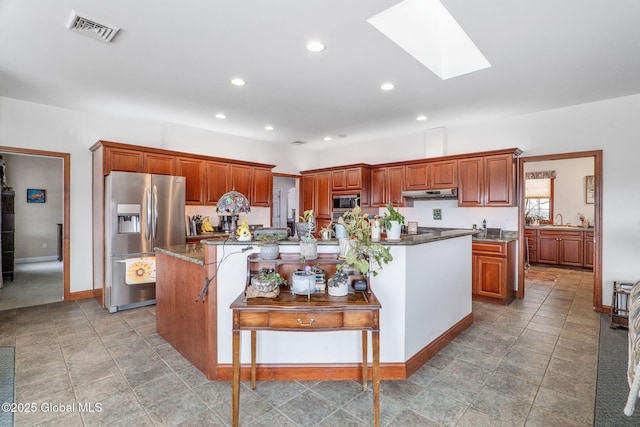 kitchen with stainless steel appliances, a skylight, an island with sink, and dark stone countertops