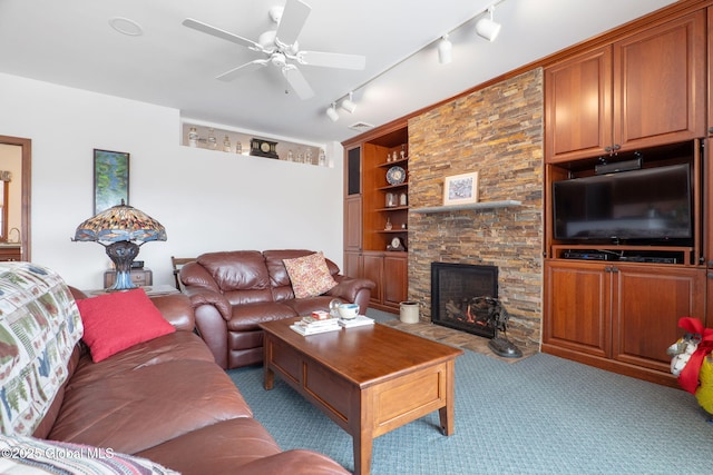 living room with built in shelves, rail lighting, a stone fireplace, light carpet, and ceiling fan