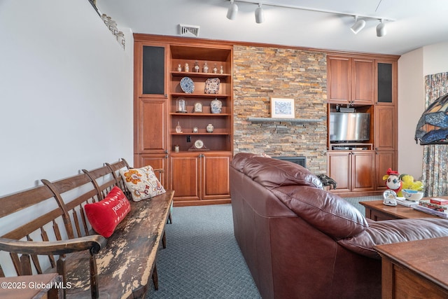 carpeted living room with rail lighting, built in features, and a fireplace