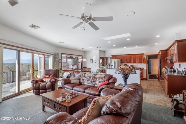 living room featuring a mountain view, a skylight, ceiling fan, and light tile patterned flooring