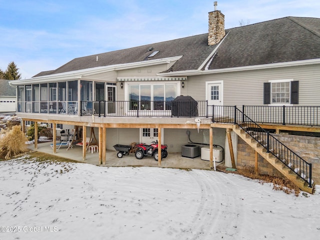 snow covered rear of property with a wooden deck, a patio area, a sunroom, and central air condition unit