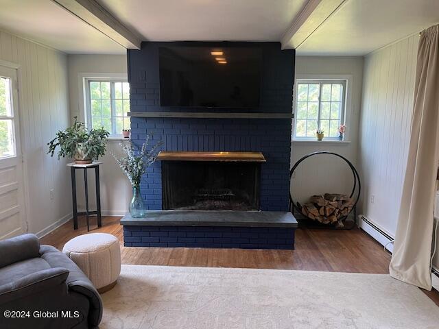 living room with a wealth of natural light, beamed ceiling, baseboard heating, and a fireplace