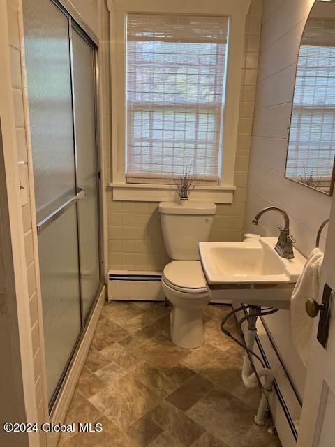 bathroom with baseboard heating, a shower with door, tile walls, sink, and toilet