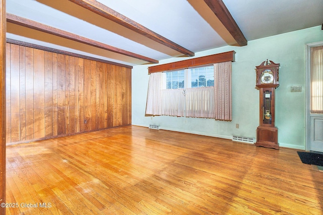 unfurnished living room featuring wooden walls, light hardwood / wood-style flooring, and beamed ceiling