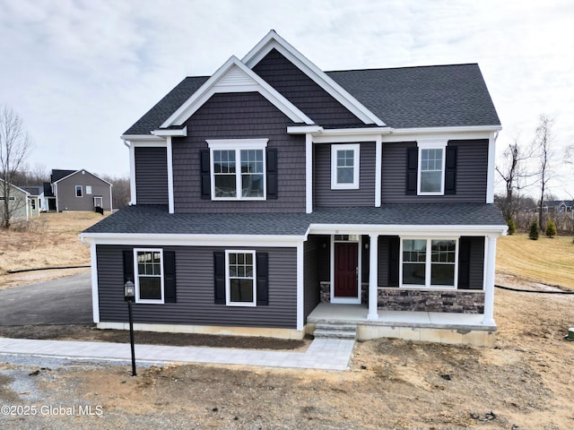 view of front of house featuring stone siding, roof with shingles, and covered porch