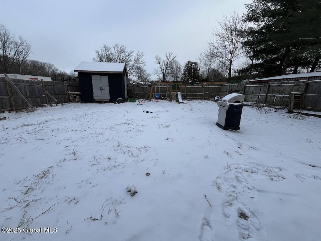 snowy yard with a playground and a storage shed