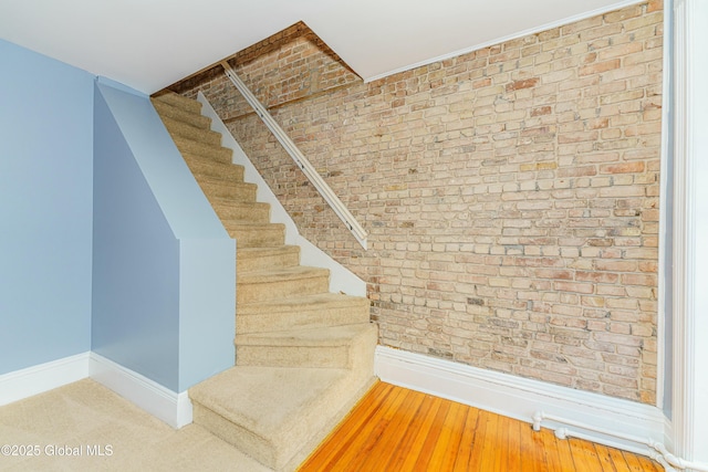 staircase with wood-type flooring and brick wall