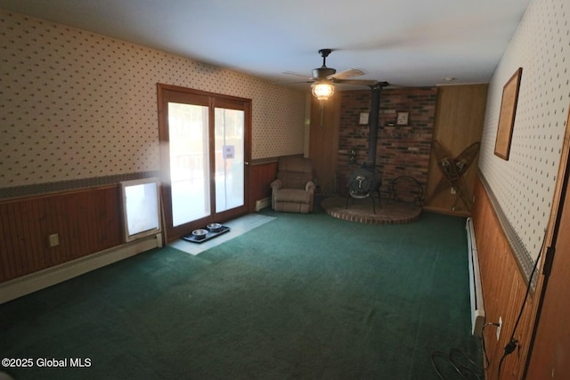 unfurnished room featuring ceiling fan, wooden walls, a wood stove, and dark colored carpet