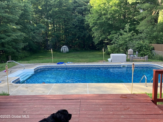 view of swimming pool with a lawn, a storage shed, and a wooden deck