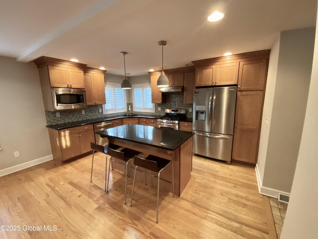 kitchen featuring decorative light fixtures, light wood-type flooring, decorative backsplash, and appliances with stainless steel finishes