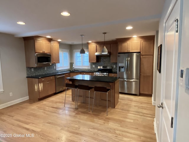 kitchen with a kitchen island, stainless steel appliances, a kitchen bar, decorative light fixtures, and light wood-type flooring