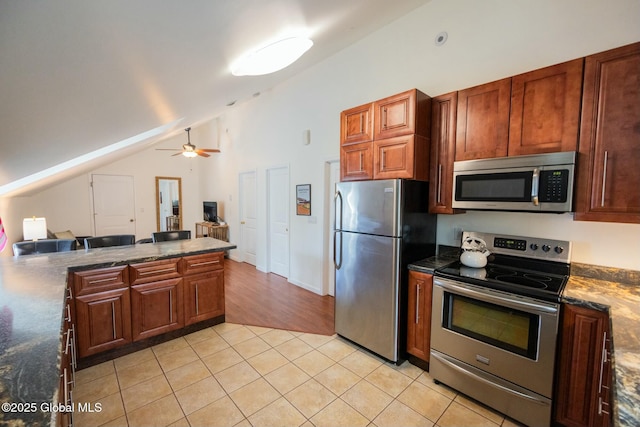 kitchen featuring light tile patterned flooring, vaulted ceiling, dark stone countertops, ceiling fan, and stainless steel appliances