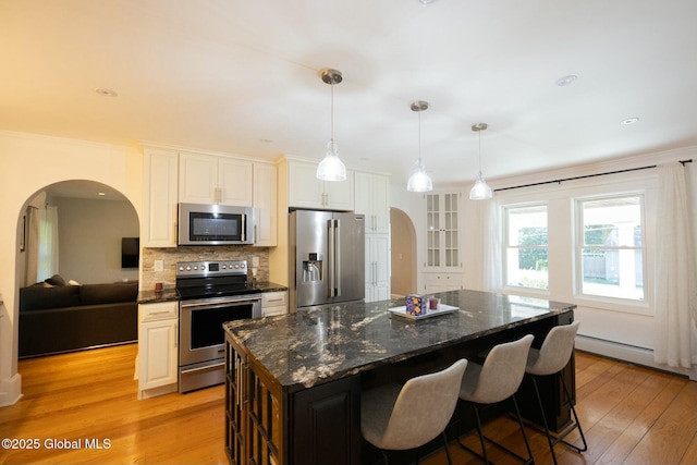 kitchen featuring decorative light fixtures, a center island, light wood-type flooring, stainless steel appliances, and white cabinets