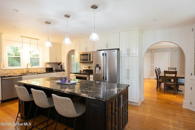 kitchen with tasteful backsplash, white cabinetry, light wood-type flooring, appliances with stainless steel finishes, and a kitchen island