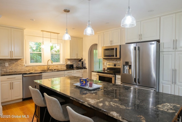 kitchen featuring appliances with stainless steel finishes, decorative light fixtures, white cabinetry, sink, and dark stone counters