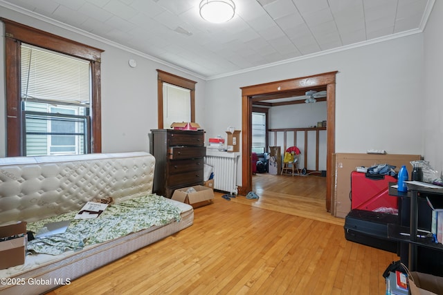 bedroom with multiple windows, ornamental molding, radiator heating unit, and light hardwood / wood-style flooring