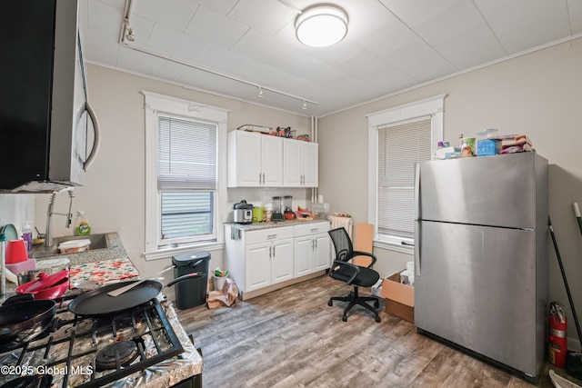 kitchen with appliances with stainless steel finishes, rail lighting, white cabinetry, crown molding, and light hardwood / wood-style flooring