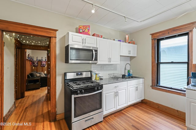 kitchen with sink, rail lighting, white cabinetry, backsplash, and stainless steel appliances