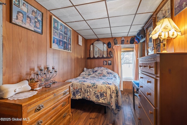 bedroom featuring a paneled ceiling, wood-type flooring, and wooden walls