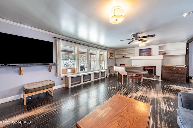 living room with built in shelves, dark hardwood / wood-style flooring, ceiling fan, a brick fireplace, and crown molding