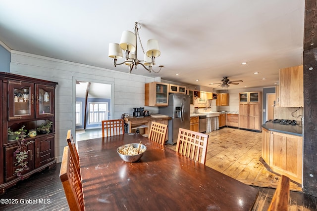 dining room with ceiling fan with notable chandelier, hardwood / wood-style floors, and wooden walls