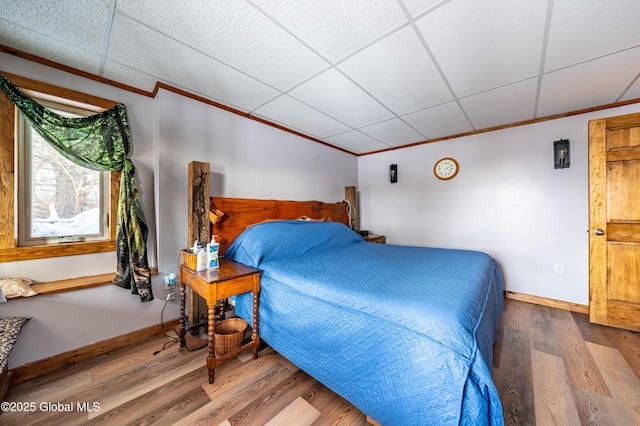 bedroom with wood-type flooring, ornamental molding, and a drop ceiling