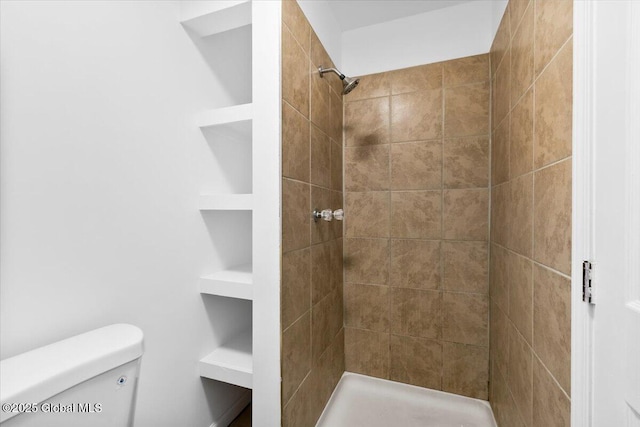 bathroom featuring toilet, built in shelves, and tiled shower