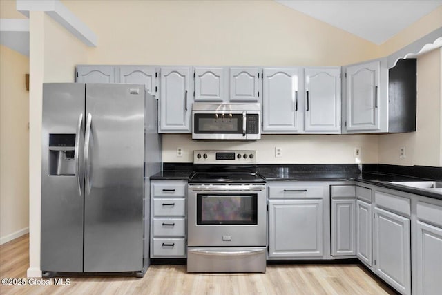 kitchen with vaulted ceiling, gray cabinetry, light wood-type flooring, sink, and stainless steel appliances