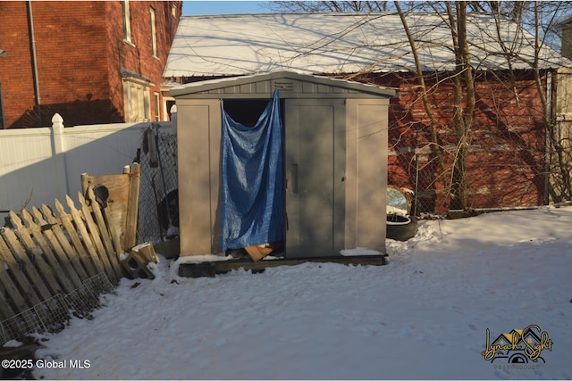snow covered structure featuring fence, an outbuilding, and a storage shed