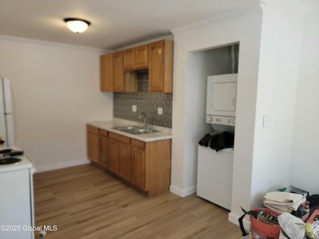 kitchen featuring sink, light hardwood / wood-style flooring, ornamental molding, stacked washing maching and dryer, and stove