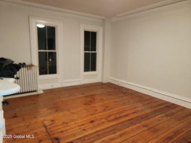 empty room with radiator heating unit, wood-type flooring, and ornamental molding