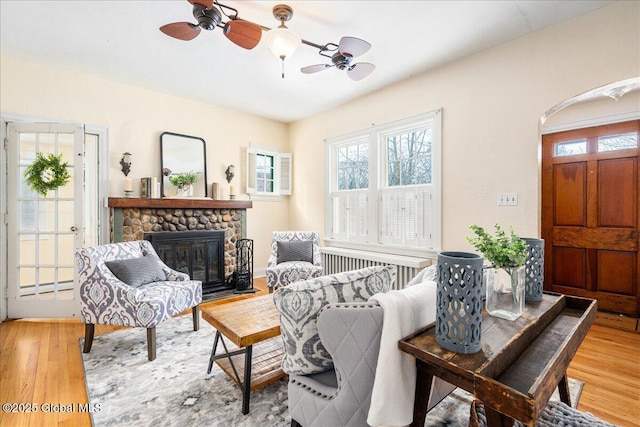 living room featuring a baseboard radiator, ceiling fan, a fireplace, and light hardwood / wood-style floors