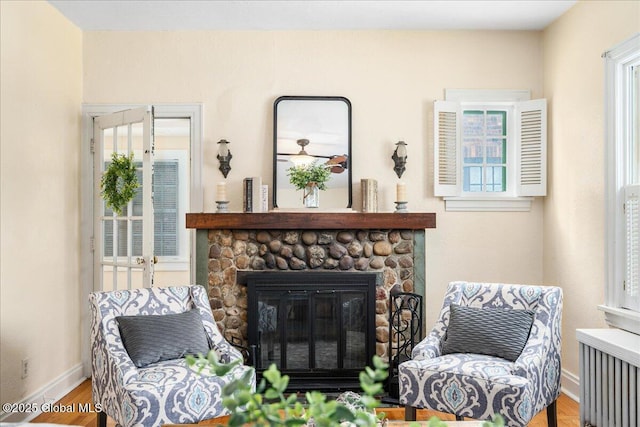 sitting room featuring radiator heating unit, a stone fireplace, and hardwood / wood-style floors