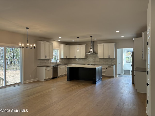 kitchen featuring white cabinetry, fridge, stainless steel dishwasher, pendant lighting, and wall chimney range hood