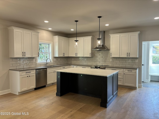 kitchen with wall chimney exhaust hood, decorative light fixtures, light hardwood / wood-style flooring, stainless steel appliances, and white cabinets