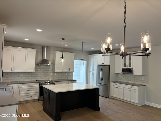 kitchen with white cabinetry, hanging light fixtures, stainless steel appliances, a kitchen island, and wall chimney exhaust hood