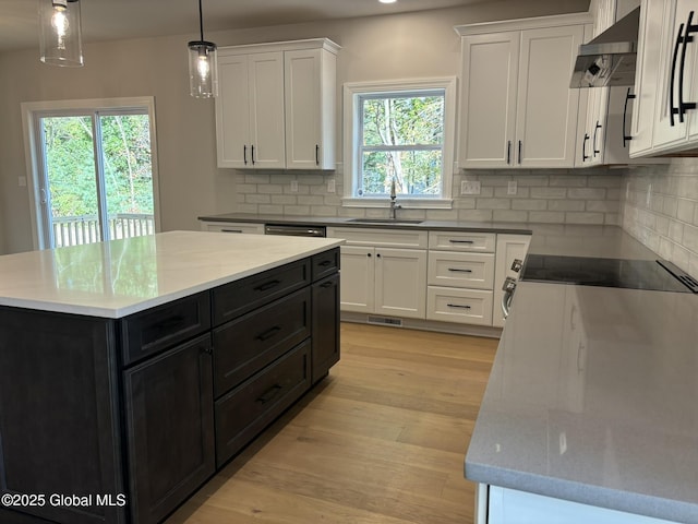 kitchen featuring a kitchen island, white cabinetry, sink, hanging light fixtures, and wall chimney exhaust hood