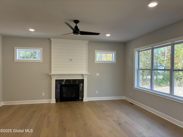 unfurnished living room with a tiled fireplace, ceiling fan, and light wood-type flooring