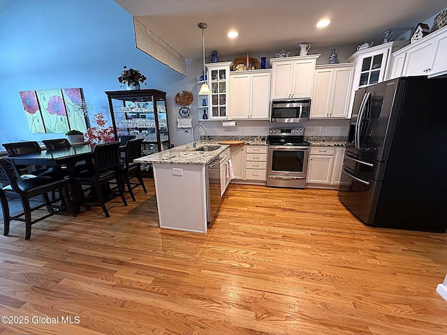 kitchen with appliances with stainless steel finishes, white cabinets, sink, pendant lighting, and light stone counters