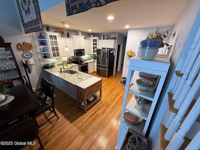 kitchen with pendant lighting, white cabinets, appliances with stainless steel finishes, light hardwood / wood-style floors, and sink