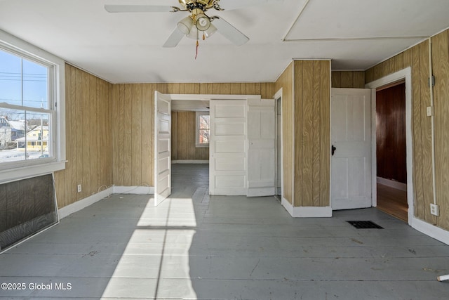 empty room featuring ceiling fan, light wood-type flooring, and wood walls