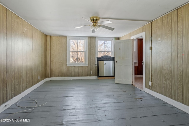 empty room with light hardwood / wood-style flooring, ceiling fan, and wood walls