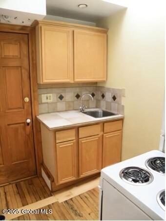 kitchen featuring backsplash, white range with electric cooktop, sink, and light wood-type flooring