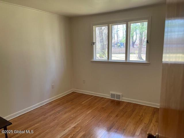 spare room featuring crown molding, baseboards, wood finished floors, and visible vents