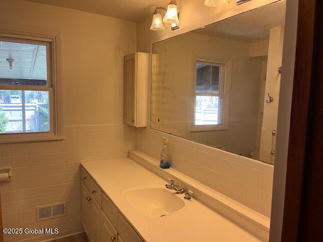 bathroom with vanity, tile walls, a healthy amount of sunlight, and visible vents