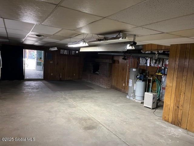below grade area featuring water heater, a drop ceiling, and wood walls