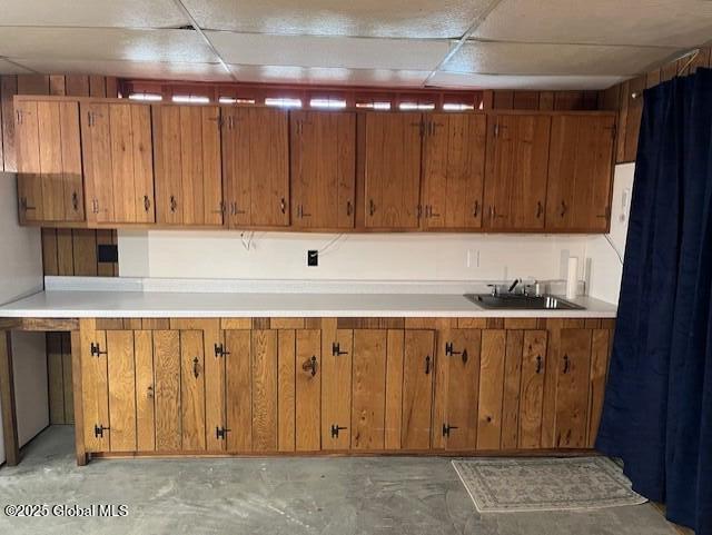 kitchen featuring a drop ceiling, brown cabinetry, and a sink