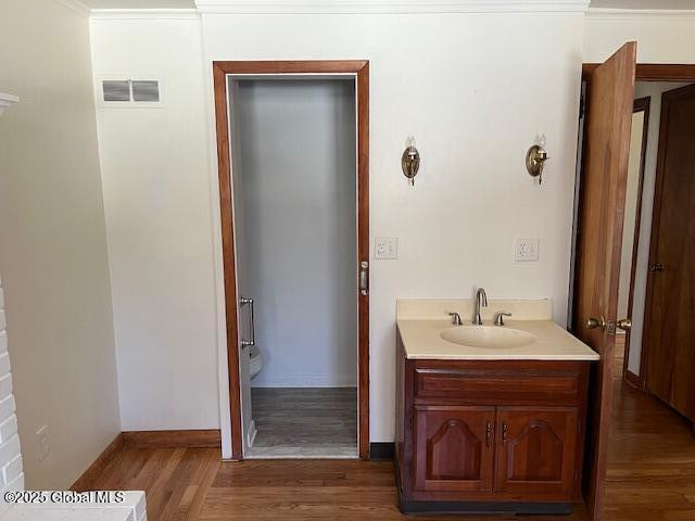 bathroom featuring vanity, toilet, baseboards, wood finished floors, and visible vents