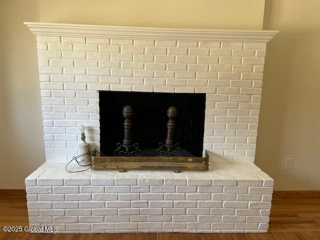 interior details featuring baseboards, a brick fireplace, and wood finished floors