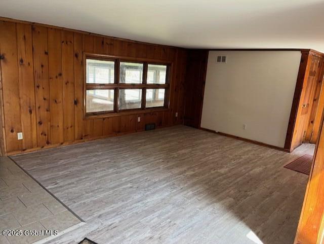 unfurnished room with wooden walls, baseboards, wood finished floors, and visible vents